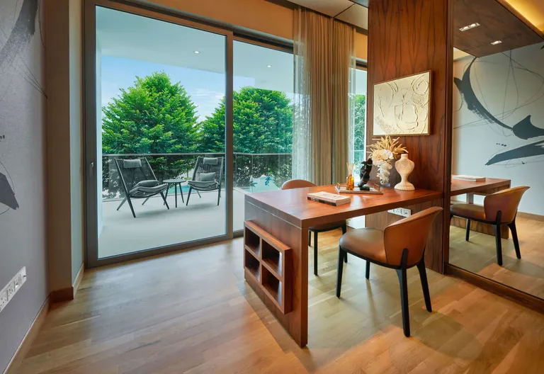 The Residences at W Sentosa Cove, photograph: a bedroom set up as a study, a timber desk and leather chairs beside a sliding door to a balcony with trees beyond