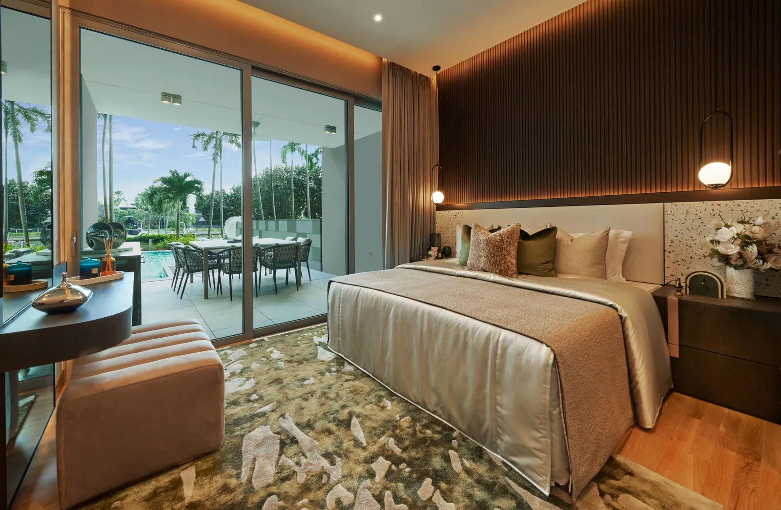 The Residences at W Sentosa Cove, photograph: a master bedroom with timber floor and a sliding glass wall opening to a terrace, a pool and palms beyond